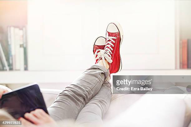 woman relaxing on sofa with tablet. - pés cruzados - fotografias e filmes do acervo