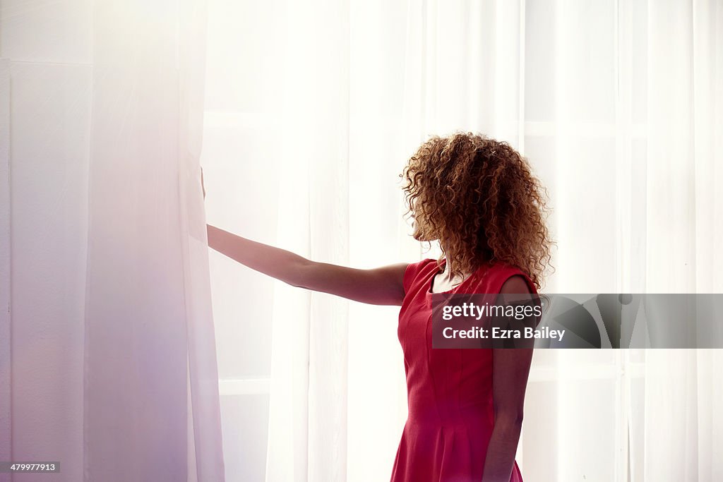 Mixed race woman looking through her window.