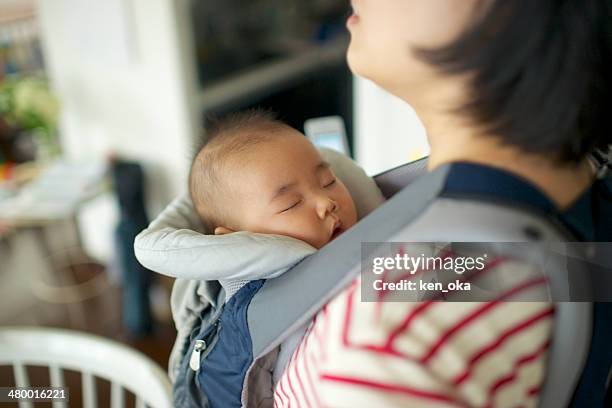 a baby sleeping in the baby carrier weared her mom - portabebés fotografías e imágenes de stock