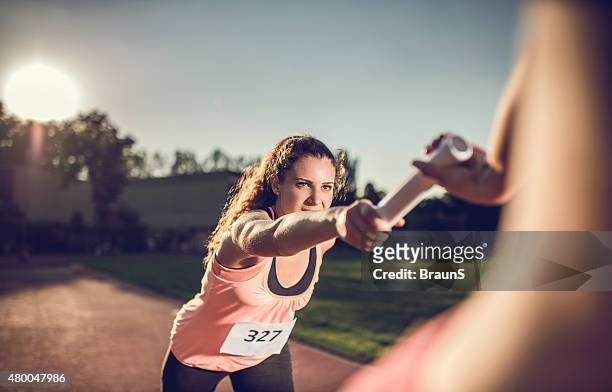 woman exchanging relay baton with her teammate on a race. - een pass geven stockfoto's en -beelden