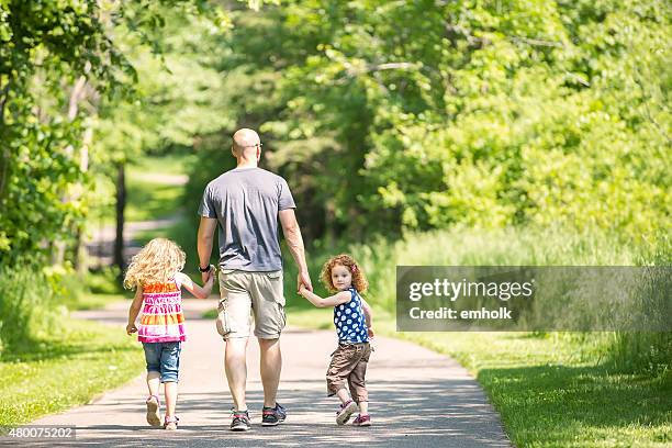 father & two daughters walking through wooded park trail - asphalt stock pictures, royalty-free photos & images