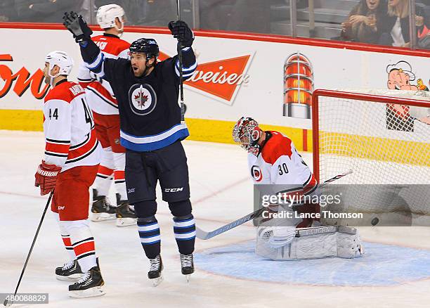 Eric Tangradi of the Winnipeg Jets throws his arms up in celebration as the puck lays in the net behind goaltender Cam Ward of the Carolina...