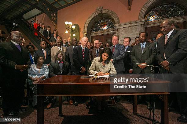South Carolina Gov. Nikki Haley, surrounded by three former governors, some family members of the slain nine and many legislators, signs the bill to...