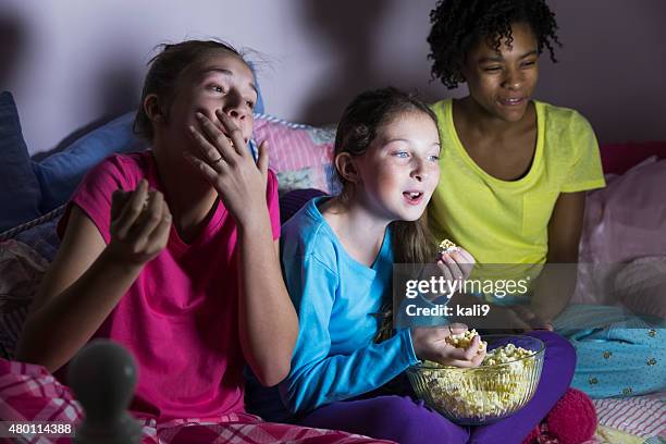 preteen mädchen im sleepover vor dem fernseher und essen popcorn - übernachtungsparty stock-fotos und bilder