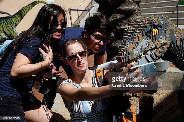 Attendees take a "selfie" photograph with a sculpture of a "Jurassic World" dinosaur made of Lego bricks during the Comic-Con International...
