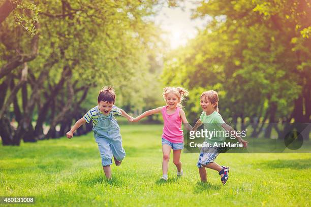 drei glückliche kinder im sommer - laufen und gras und sport stock-fotos und bilder