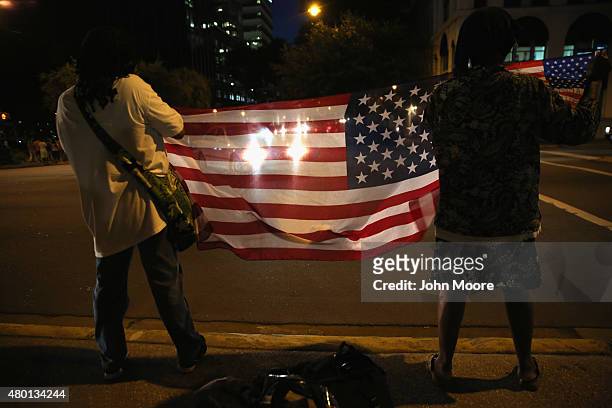 People hold the American flag as the Confederate "Stars and Bars" flies in front of the South Carolina statehouse on its last evening on July 9, 2015...
