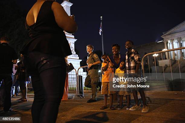 People pose for photos as the Confederate "Stars and Bars" flies in front of the South Carolina statehouse on its last evening on July 9, 2015 in...
