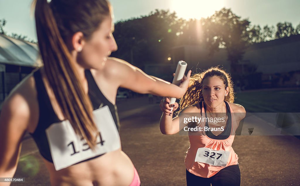 Female athletes exchanging baton on a relay race.