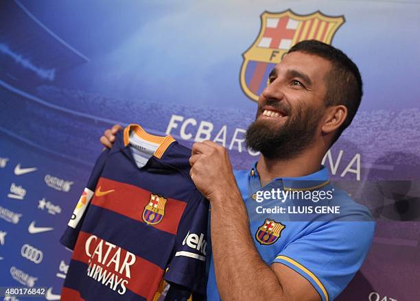 Barcelona's new player Turkish Arda Turan smiles as he shows his new jersey at the Camp Nou stadium in Barcelona, after signing his new contract with...