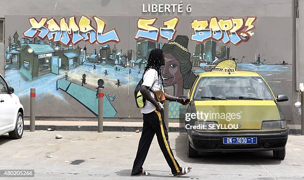 People walk past a wall bearing graffiti in Dakar on June 26, 2015. Graffiti featuring religious figures, politicians, daily life scenes, as well as...