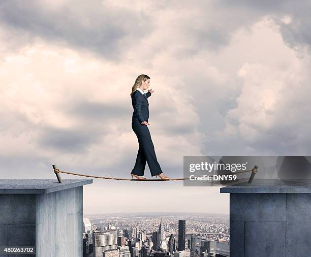 busineswosman balancing on a tightrope above big city - tightrope stockfoto's en -beelden