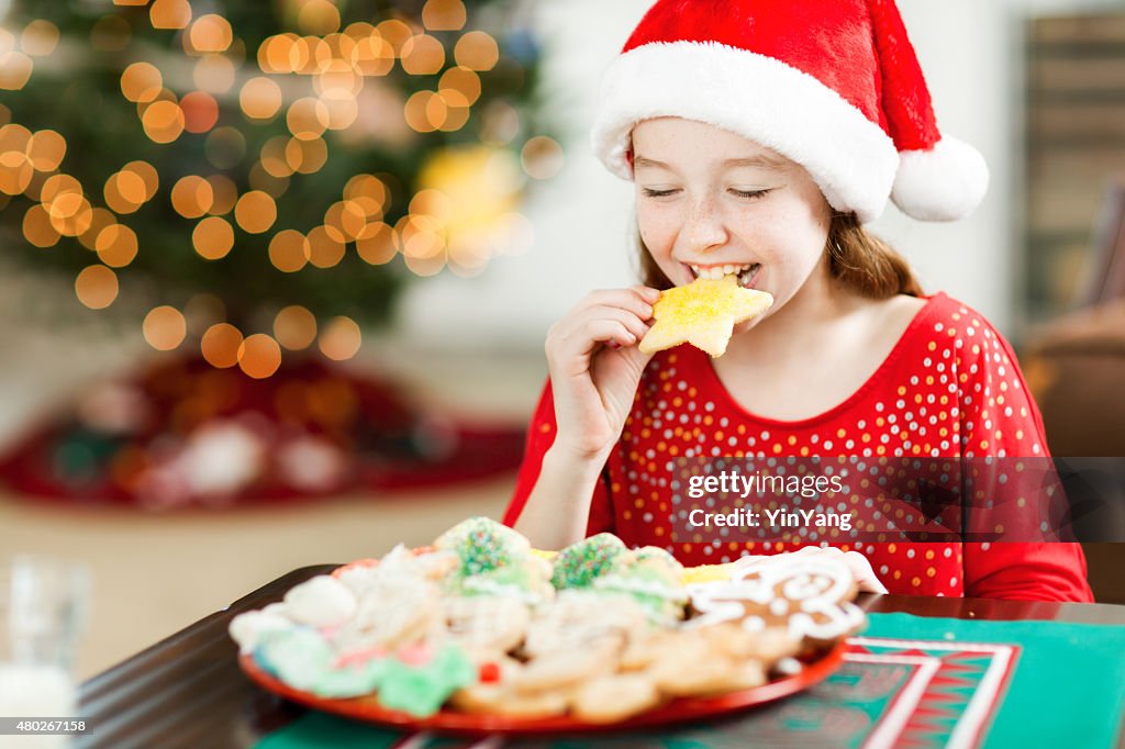 Happy Girl Eating Christmas Cookies in front of Tree Close-up