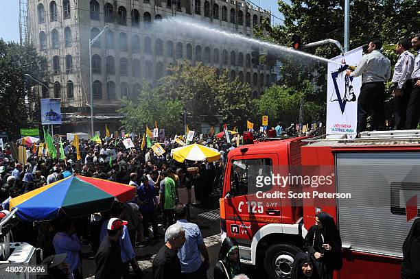 Iranian firemen spray water over the crowds to ease the summer hear as Iranians wave flags and anti-Israel posters while marching in a Qods Day...