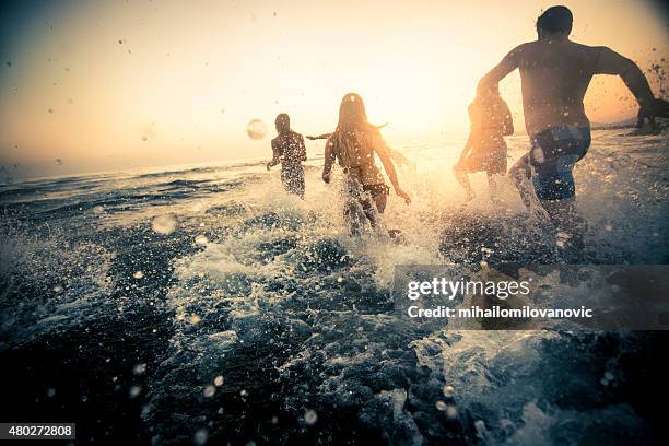 group of friends running into the water - escaping stock pictures, royalty-free photos & images