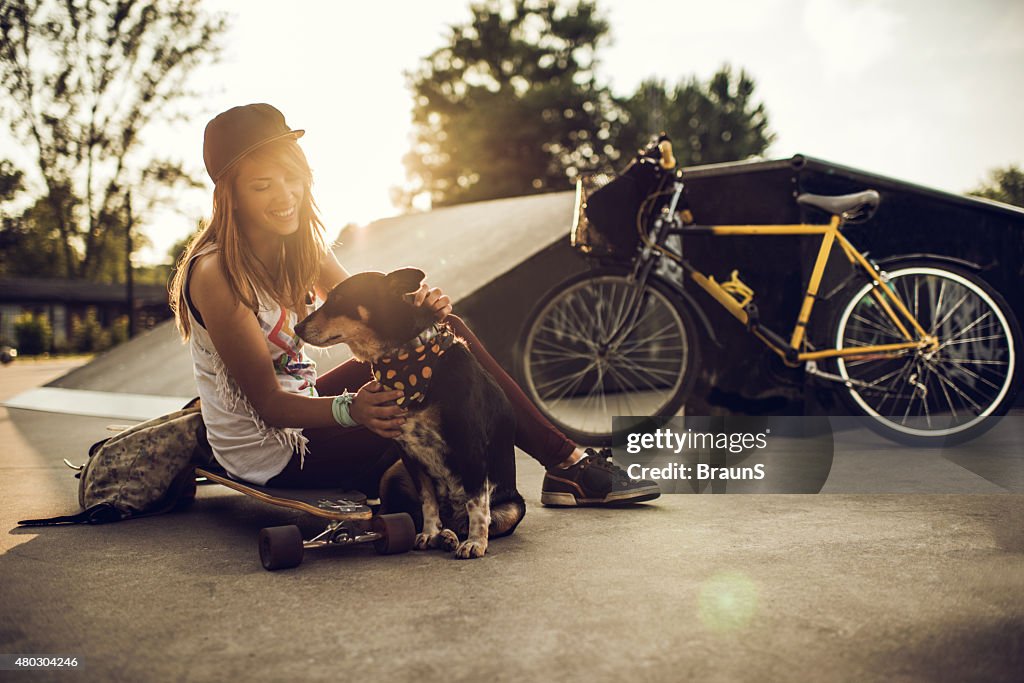 Young happy woman enjoying with dog at skate park.