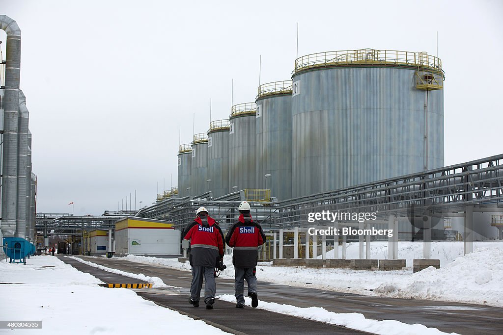 Employees walk past pipework and oil storage tanks at Royal Dutch ...