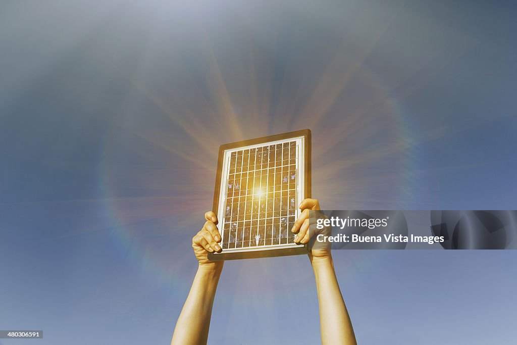 Woman's  arms lifting a solar panel  toward  the s