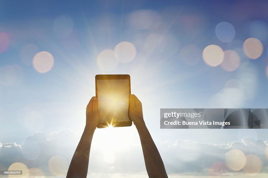 Woman's  arms pointing a tablet toward the sun
