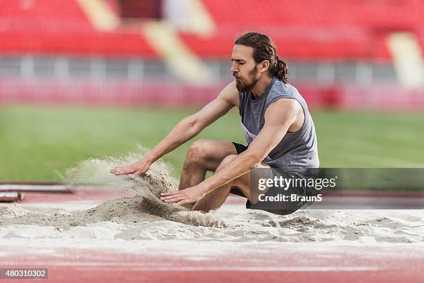 young man exercising long jumps and landing in a sand. - verspringen stockfoto's en -beelden