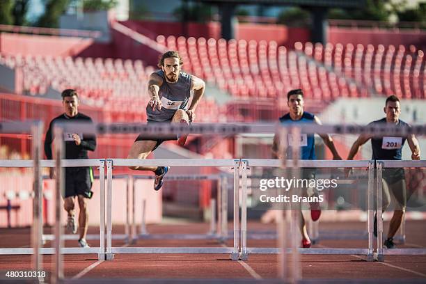 group of male athletes jumping hurdles on a race. - hurdle stock pictures, royalty-free photos & images