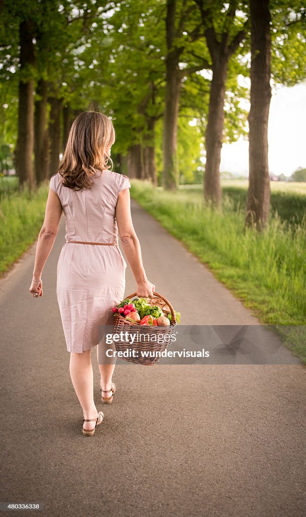 Woman walking through a park carrying a basket of vegetables