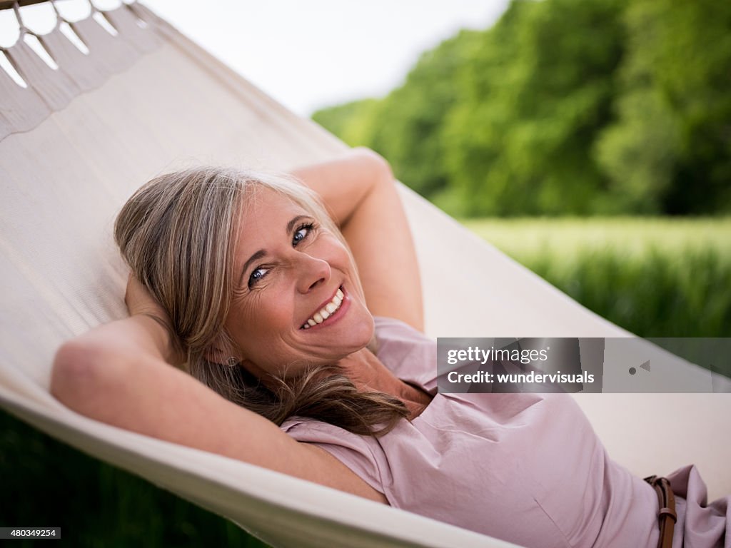 Reife Frau lächelnd fröhlich in einer Hängematte im Freien