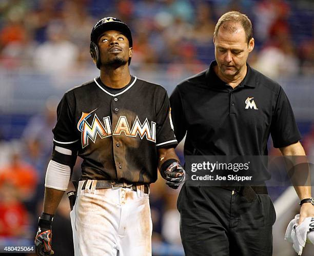 Baserunner Dee Gordon of the Miami Marlins leaves the game with a trainer after he slid safely headfirst into first base beating a tag by first...