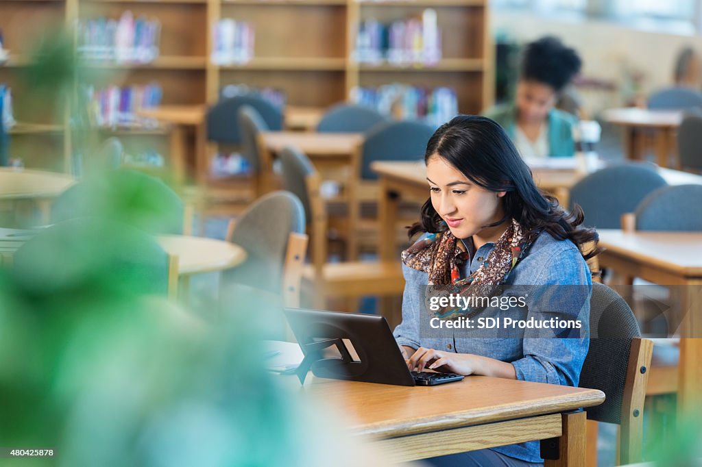 Hispanic college student using digital tablet to study in library