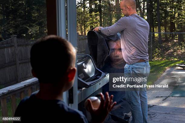 Mason Lee of Winslow, with a baseball in hand, looks out the window toward the backyard as his father, Jamie, takes the cover off the grill before...