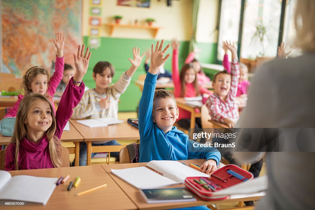 School children raising their hands ready to answer the question.