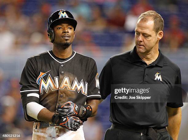 Dee Gordon of the Miami Marlins leaves the game with a trainer after sliding safely into first base, beating a tag by first baseman Manny Parra of...