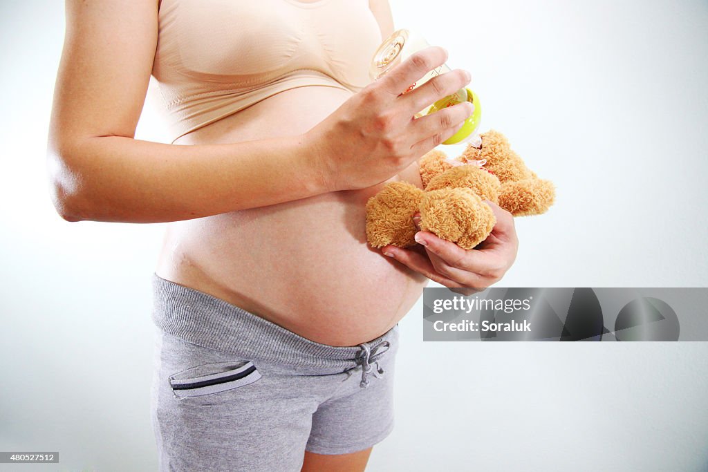 Mom in pregnancy feeding Milk a teddy bear.