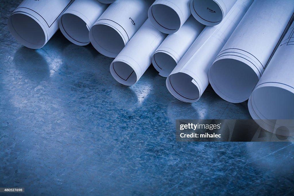 Rolls of white construction plans on scratched metallic backgrou