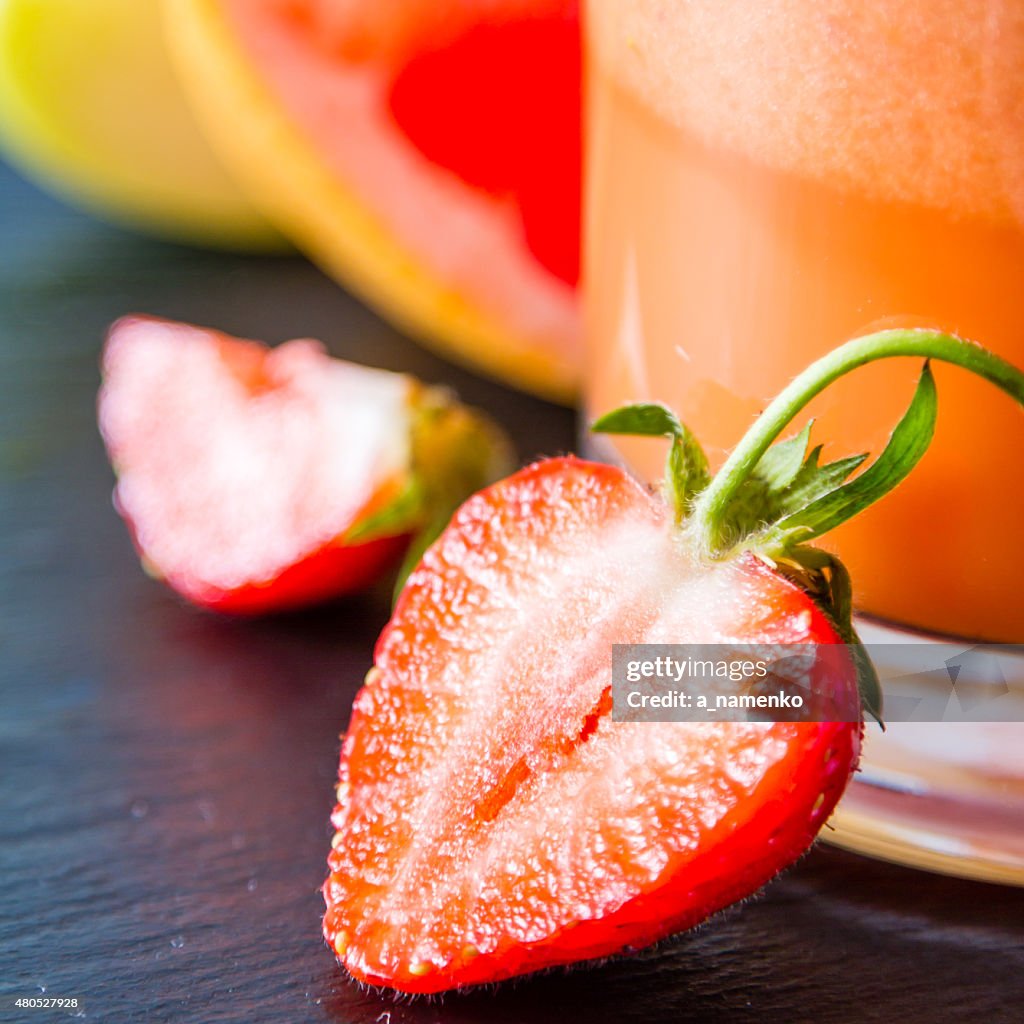 Apple, grapefruit and strawberry smoothie and ingredients, dark stone background