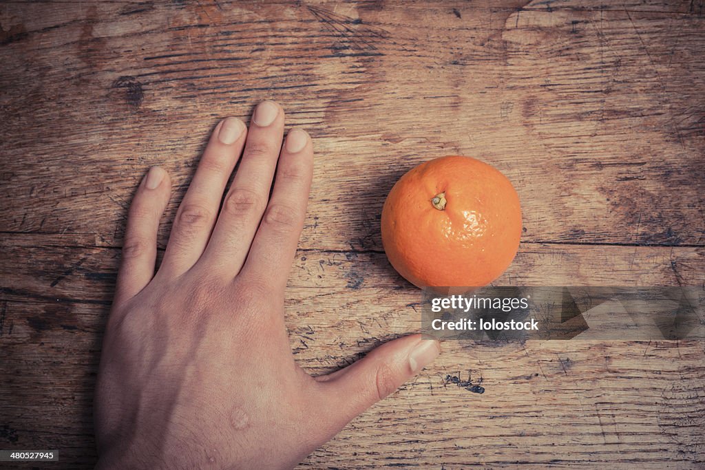 Hand and orange on table