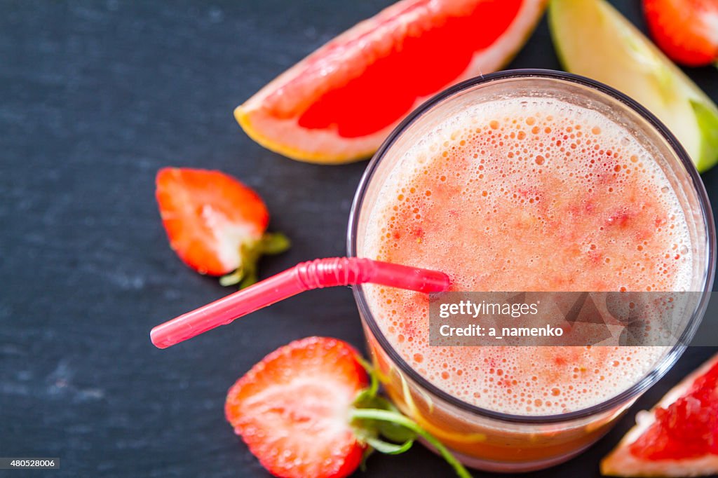 Apple, grapefruit and strawberry smoothie and ingredients, dark stone background