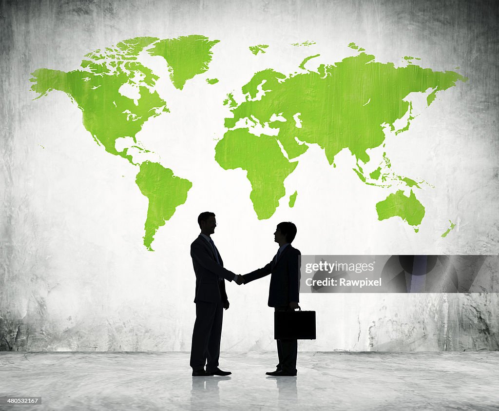 Businessmen shake hands with green land background