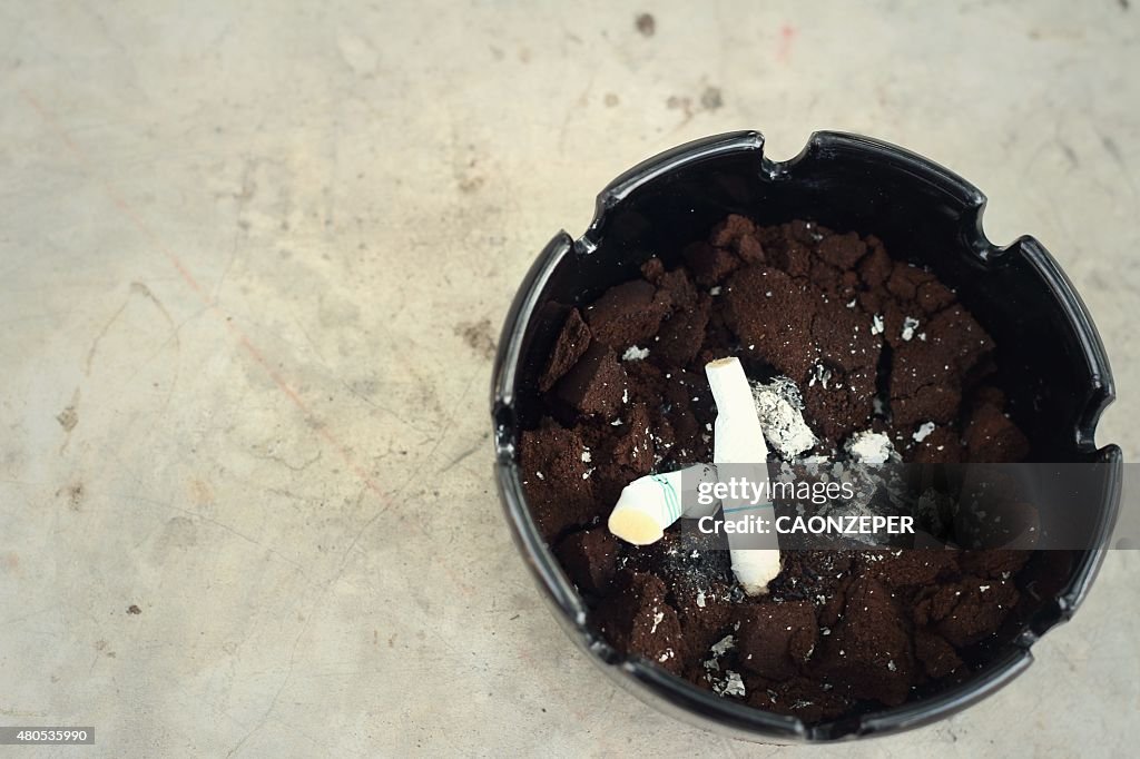 Cigarette in the ashtray on the cement floor.