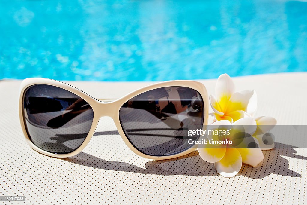 Sunglasses and plumeria flowers near the pool