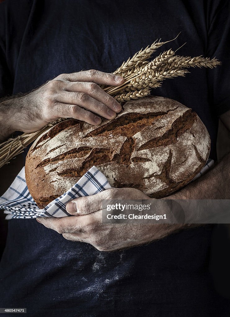 Baker man holding loaf of bread and wheat in hands