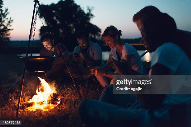 hikers using smart phones around campfire. - camping friends bildbanksfoton och bilder