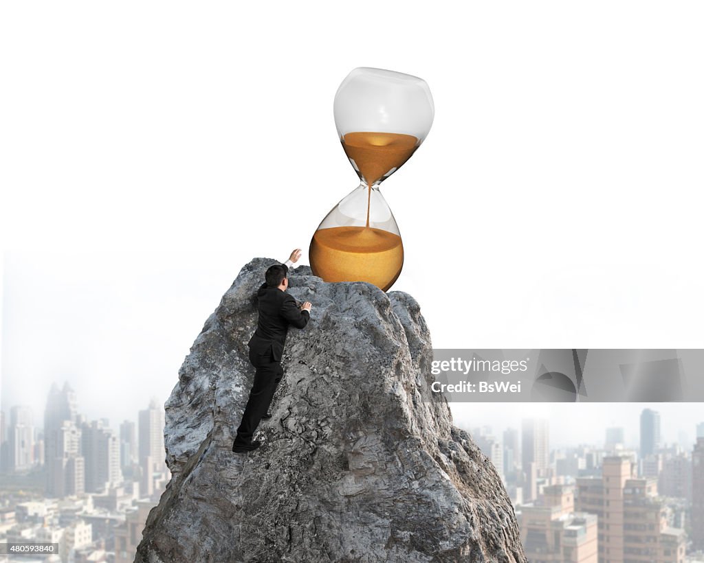 Businessman trying to grab hourglass on peak