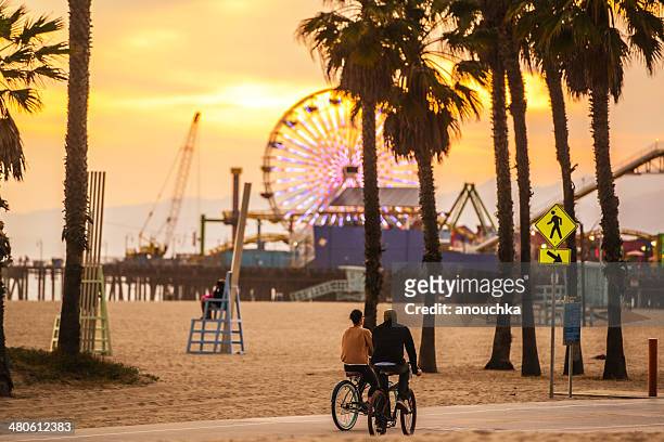 persone in bicicletta sulla spiaggia di santa monica al tramonto - santa monica pier foto e immagini stock