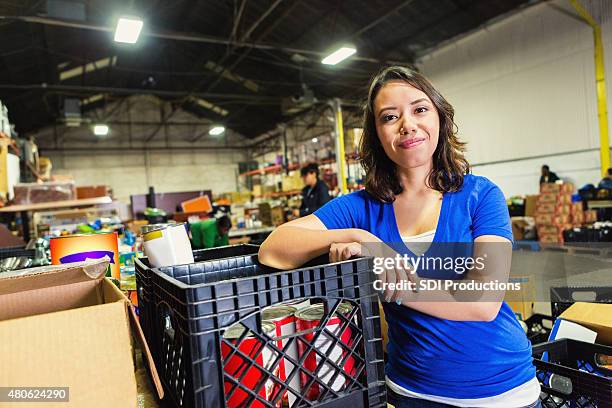 young mixed-race woman volunteering in food bank warehouse - community work space stock pictures, royalty-free photos & images