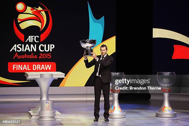 Former Socceroo Brett Emerton holds the AFC Asian Cup on stage prior to the final draw for the 2015 AFC Asian Cup draw at Sydney Opera House on March...