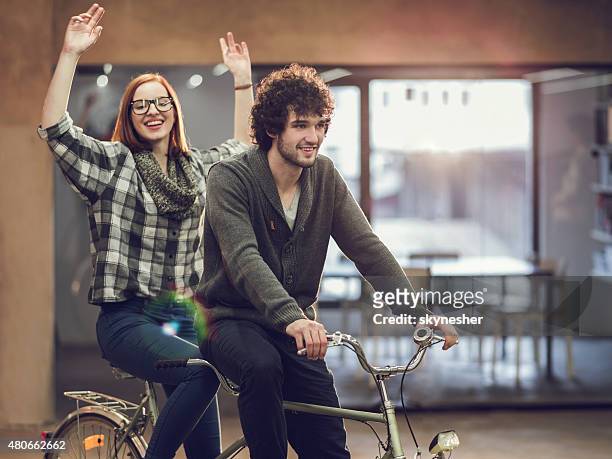 cheerful young couple on a tandem bicycle indoors. - tandem bicycle stock pictures, royalty-free photos & images