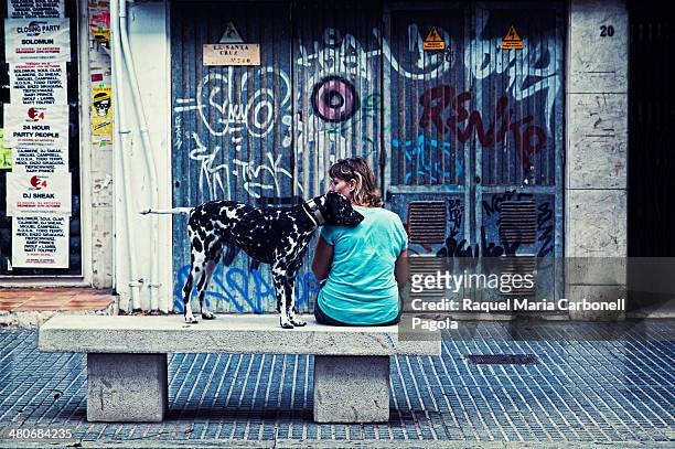 Woman and her dog sitting on a bench in city center streets.