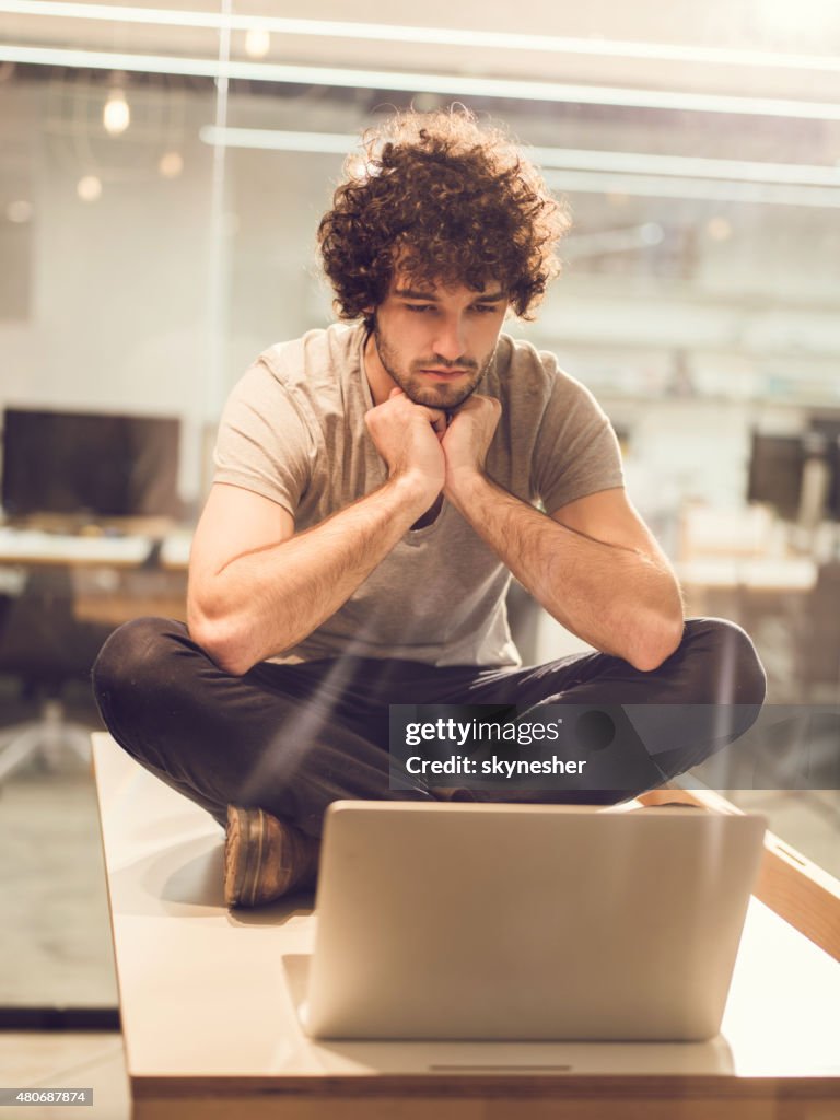 Serious young man sitting on the table and using laptop.