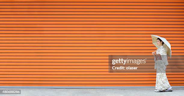 kimono woman walking in front of monochrome wall - kimono stockfoto's en -beelden